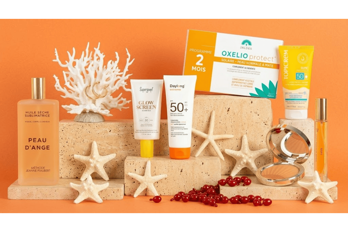 Box Marie Claire Beauté Solaire édition limitée 8 produits accessoire huile sèche Peau d'Ange Méthode Jeanne Piaubert base Supergoop Glow Screen SPF30 lait solaire Daylong SPF50 plus compléments Jaldes Oxelio Protect crème Topicrem SPF50 poudre bronzante Clarins eau de parfum Gas Bijoux La Route des Plages boucles d'oreilles dorées Nilaï corail blanc étoiles de mer capsules rouges fond orange ambiance plage été