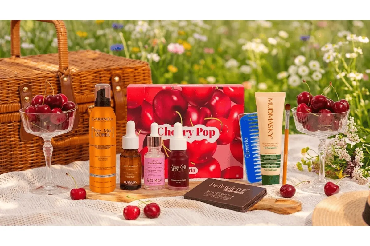 Box Glowria Cherry Pop avec les produits Garancia, Huygens, Bomoï, Sugar Silk Beauty, Mudmasky et Bellapierre disposés dans l'herbe lors d'un pique-nique champêtre